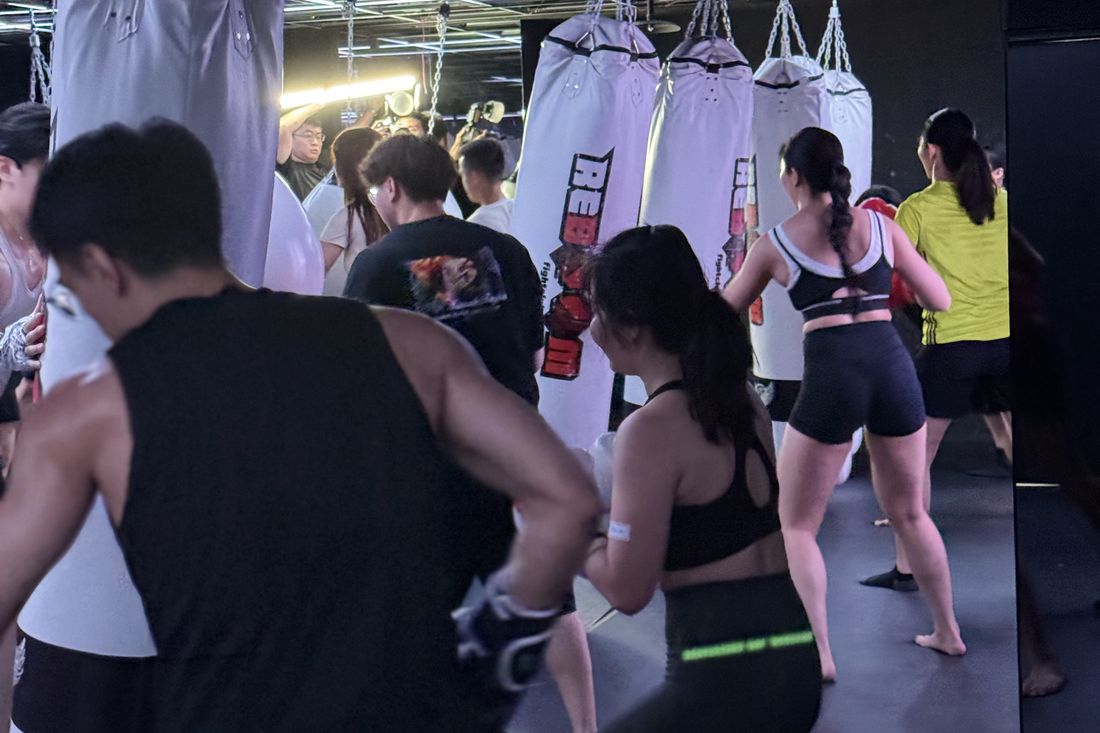 格鬥館裡一整排參加者面向沙包,跟著同一個節奏出拳,畫面多為背影